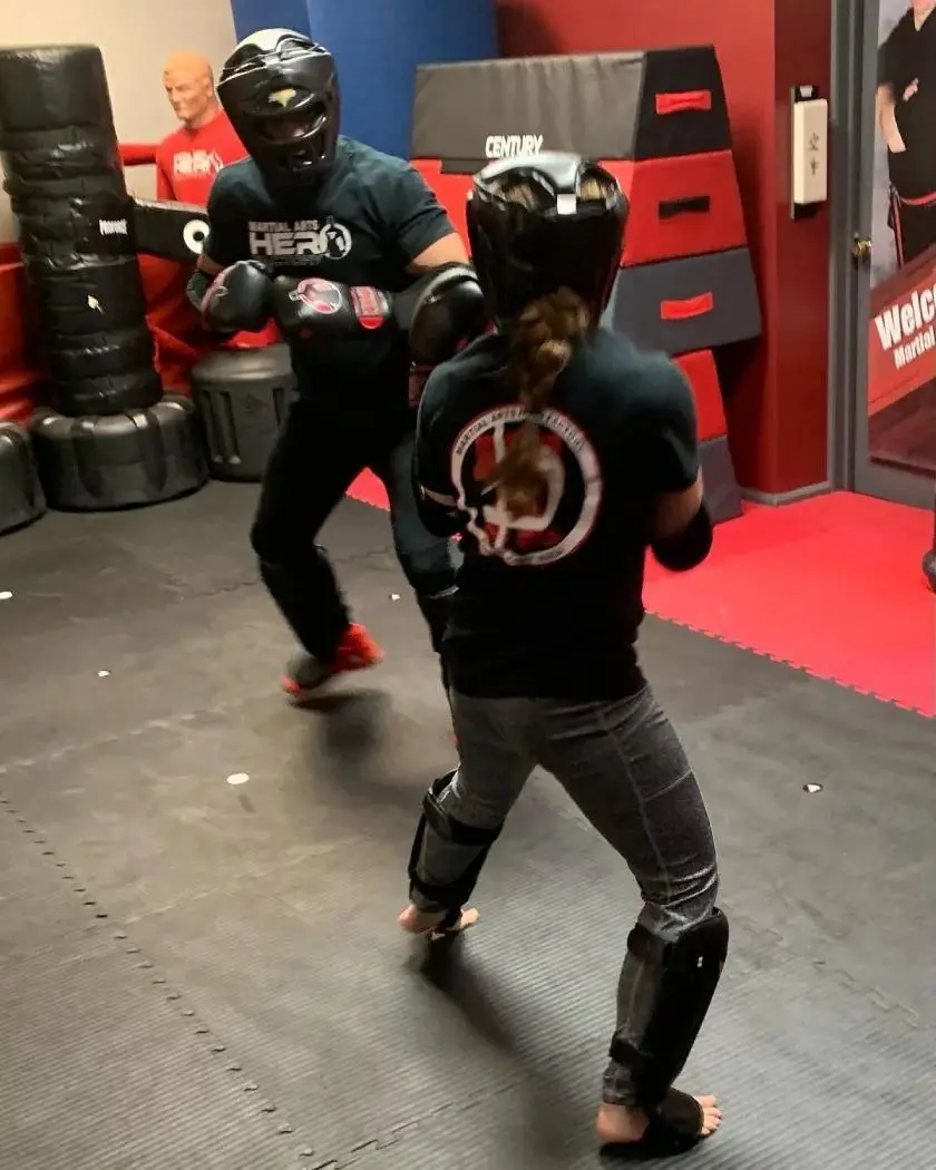 Martial arts students sparring in full protective gear on padded gym mats.
