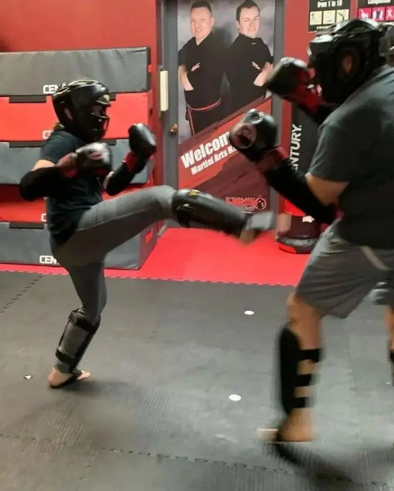 Martial arts sparring session with students wearing headgear, gloves, and shin guards.