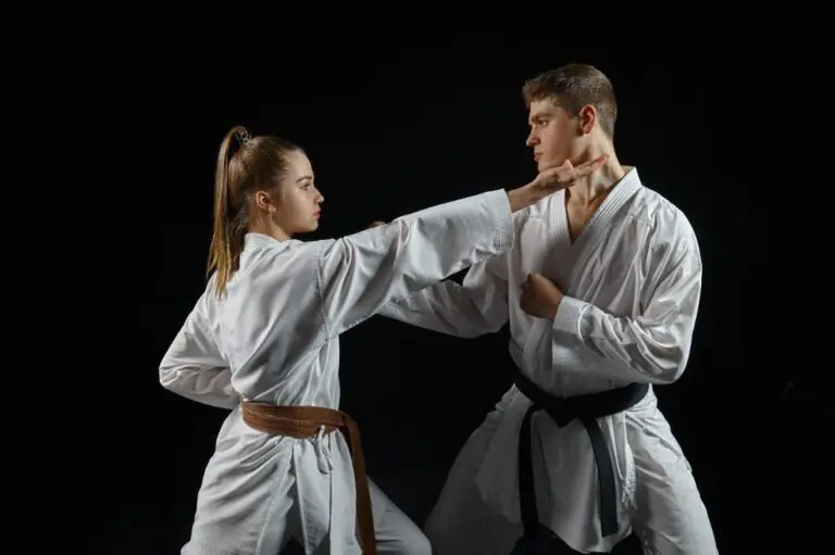 A disciplined adult martial arts moment: a female brown belt strikes the neck of her male black belt counterpart in a focused Karate sparring match, set against a black background.