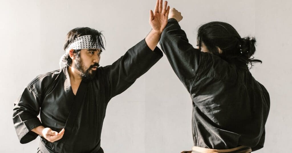A male instructor with a beard and a patterned headband demonstrates a defensive blocking technique during a session of martial arts for beginners.