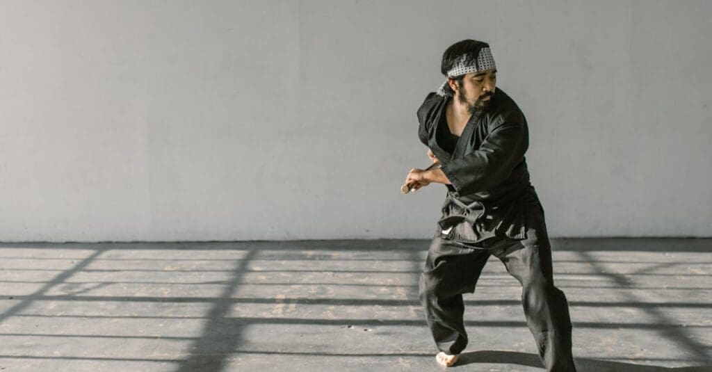 A martial artist dressed in a black gi and headband practices a low stance and hand positioning as part of their training in martial arts for beginners.